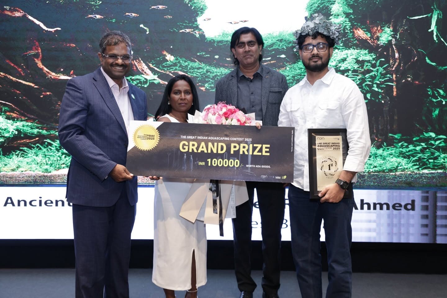 Grand prize winner felicitated on stage against a nature aquarium backdrop
